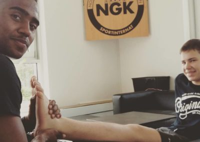 Physio-Azubi und Zehnkämpfer Ituah behandelt eine kleine Verletzung von Nachwuchs-Fechter Valentin Meka